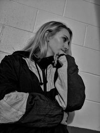 Young woman looking away while standing against wall