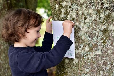 Side view of girl sticking paper on tree