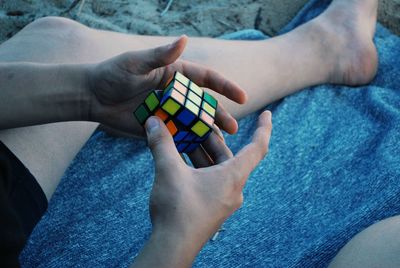 Low section of man holding puzzle cube while sitting at beach