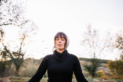 Smiling woman wearing knit hat meditating on bench at park