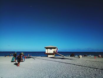 People at beach against clear blue sky