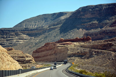 Vehicles on road by mountains against clear sky