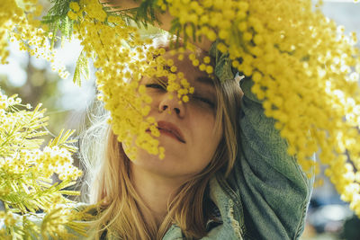 Portrait of a blonde woman with a yellow plant mimosa in spring.