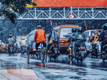 People riding vehicle on wet street in city during rainy season