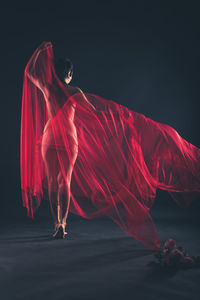 Full length of naked woman with red fabric against black background
