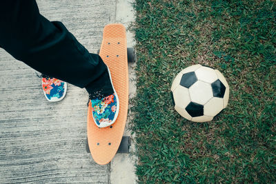 Low section of man with surfboard by soccer ball on grassy field