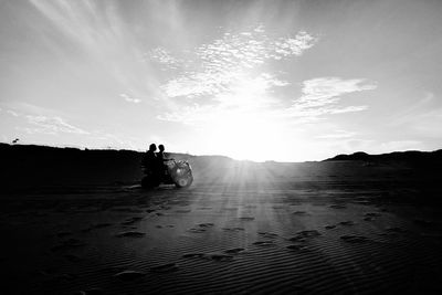 Friends riding quadbike on field against sky