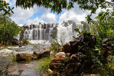 Low angle view of waterfall in forest against sky