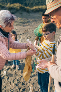 Grandmother assisting grandson while putting on protective glove while standing at beach