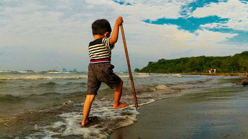 Rear view of boy on beach against sky