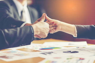 Midsection of business people showing thumbs up at office