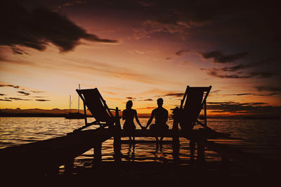 Silhouette people on pier over sea against sky during sunset