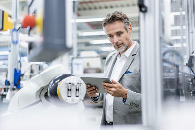 Businessman with tablet at assembly robot in a factory