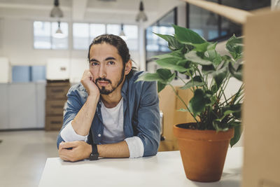 Portrait of young businessman with hand on chin sitting at table in new office