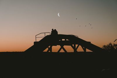 Silhouette man flying bird against sky during sunset