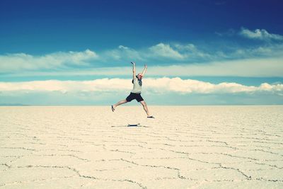 Full length of man with arms raised at salar de uyuni against sky