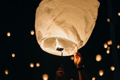 Low angle view of person holding illuminated lantern against sky