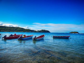 Boats moored in sea against blue sky