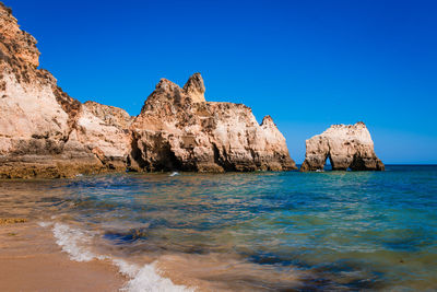 Rock formations in sea against clear blue sky