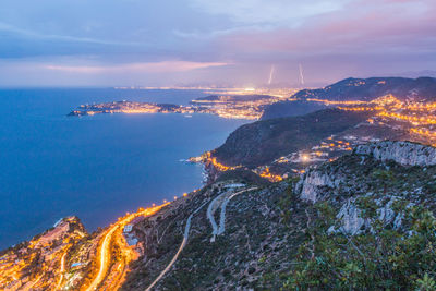 Lightning over illuminated city by sea