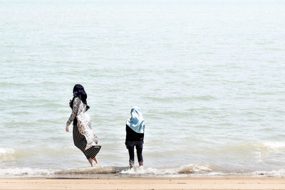 Rear view of girl standing by woman levitating on shore at beach