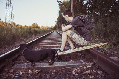 Young man with dog sitting on railroad track