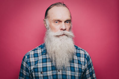 Portrait of serious senior man with long white beard against pink background