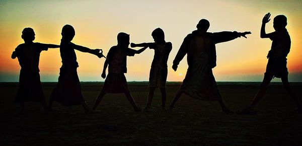 Silhouette boys practicing karate at beach during sunset