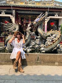 Full length of woman wearing hat sitting on retaining wall