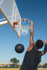 Back view of powerful energetic african american sportsman hanging on basketball lap after scoring ball in net on playground