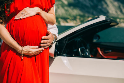 Cropped hand of man touching stomach of pregnant woman by car