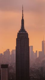 Empire state building in city against orange sky during sunset