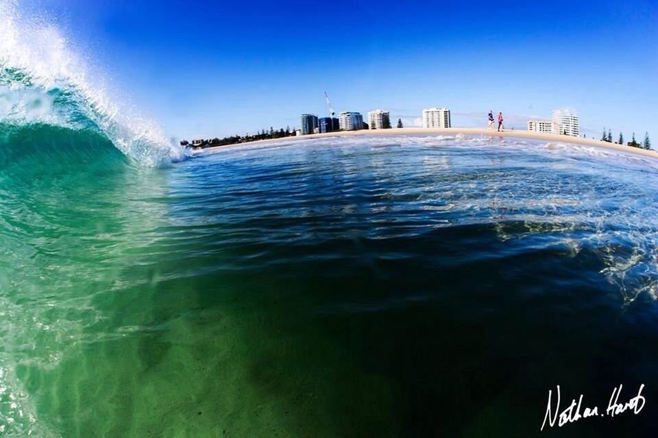 water, blue, sea, clear sky, built structure, architecture, building exterior, waterfront, wave, city, rippled, surf, copy space, turquoise colored, beach, day, nature, motion, beauty in nature, incidental people