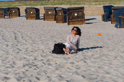Woman sitting on sandy beach with hooded chairs in background