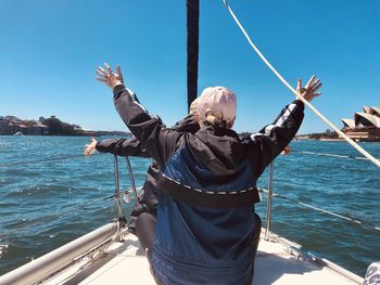 Rear view of man standing on boat in sea against sky