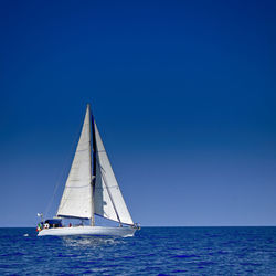 Sailboat sailing in sea against clear blue sky