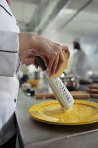 Midsection of chef grating cheese in kitchen