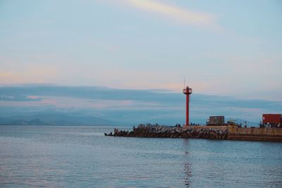 Lighthouse on sea against buildings during sunset