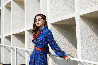 Young woman wearing sunglasses standing against wall