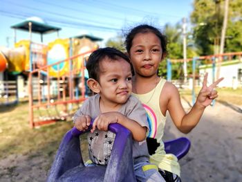 Portrait of sister with brother sitting on outdoor play equipment in playground