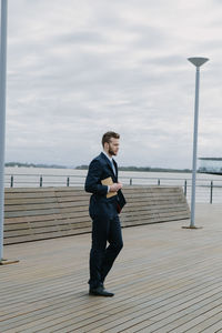 Side view of young man standing on sea against sky