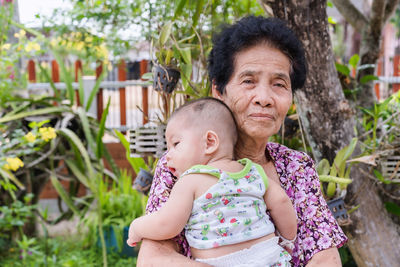 Happy senior woman holding adorable baby boy in spring flowery garden. grandmother holding newborn