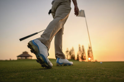 Low section of men on golf course against sky during sunset