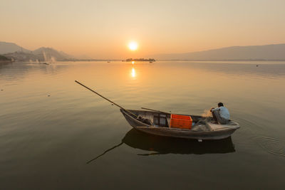 Side view of man traveling in boat on sea against sky during sunset