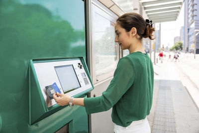 Smiling woman operating ticket machine with credit card at tram stop