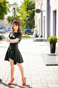 Beautiful young woman in black dress standing on sidewalk in city