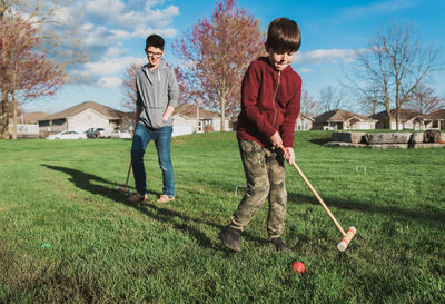 Two boys playing a game of croquet in a park together.