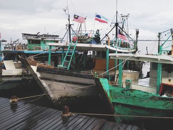 Fishing boats moored at harbor against sky