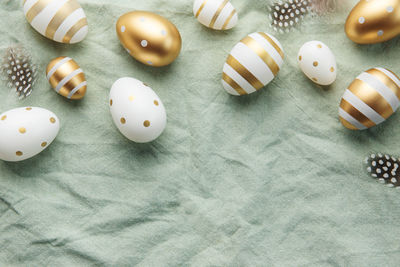 Easter eggs are painted with gold paint on a green linen background. 