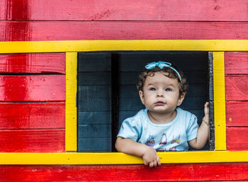 Cute baby girl looking through window while standing in wooden playhouse